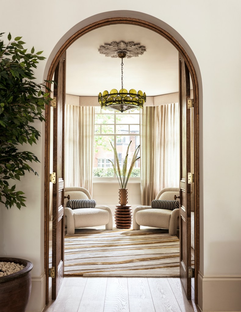 Interior view of a cozy living room featuring two stylish armchairs with striped cushions, a decorative vase with plants, and a striking chandelier hanging from a textured ceiling, framed by an arched doorway.