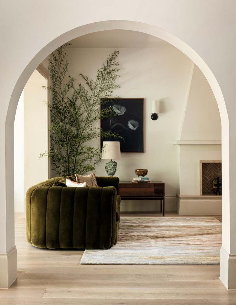 A well-decorated living space featuring a plush green sofa, a potted plant, and a dark artwork on the wall, framed by an elegant archway.